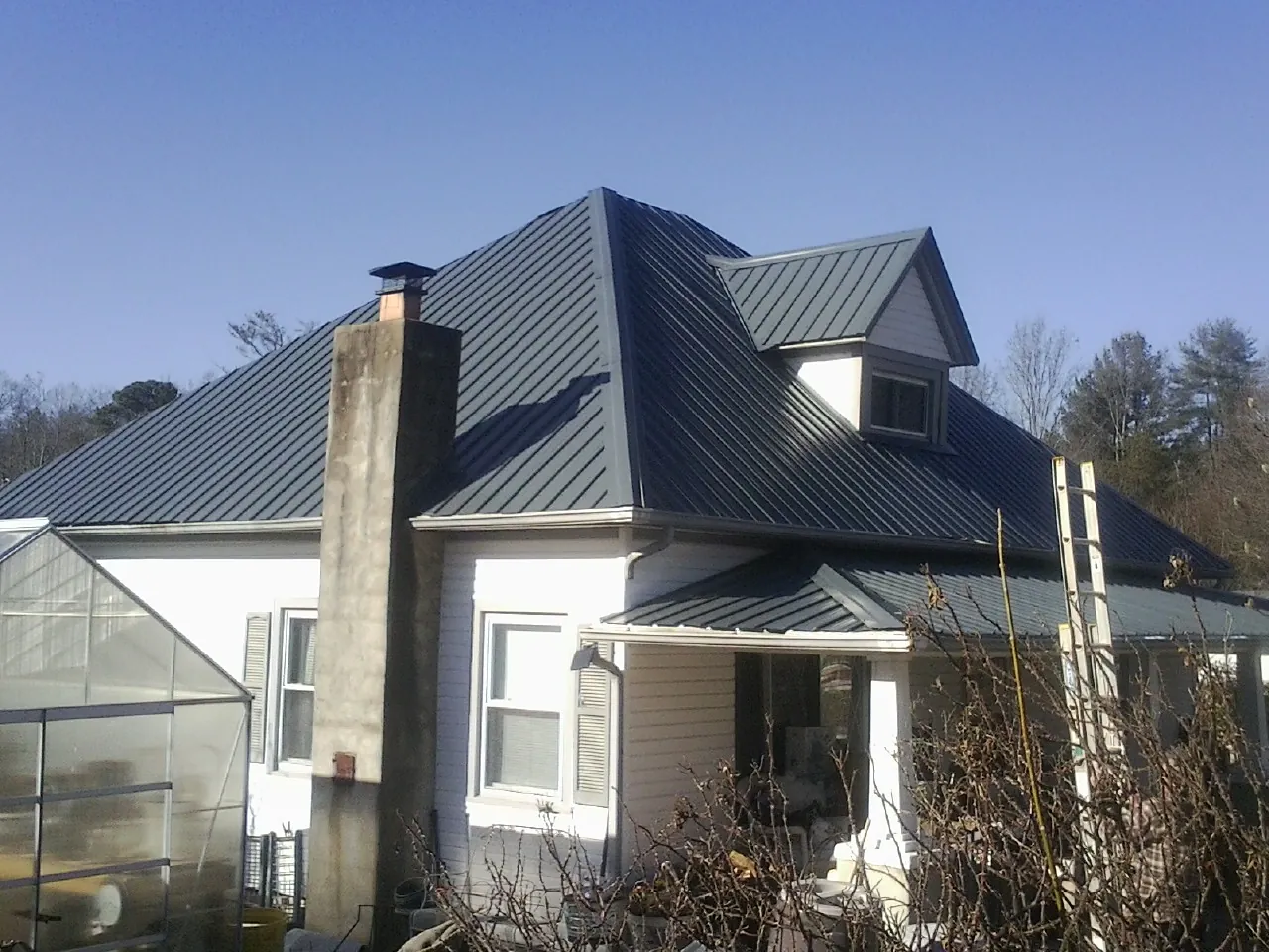 Dark blue standing seam metal roof on a white farmhouse with dormer — Slate & Tile Roof Repair by Roofing Brothers in Tussy