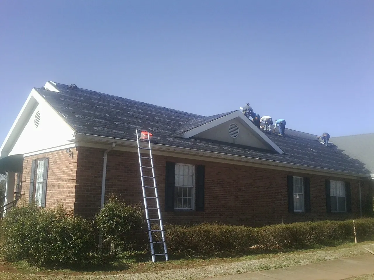 Crew tearing shingles off a brick ranch roof with a ladder set — Metal Roof Repair work by our crew in Tussy