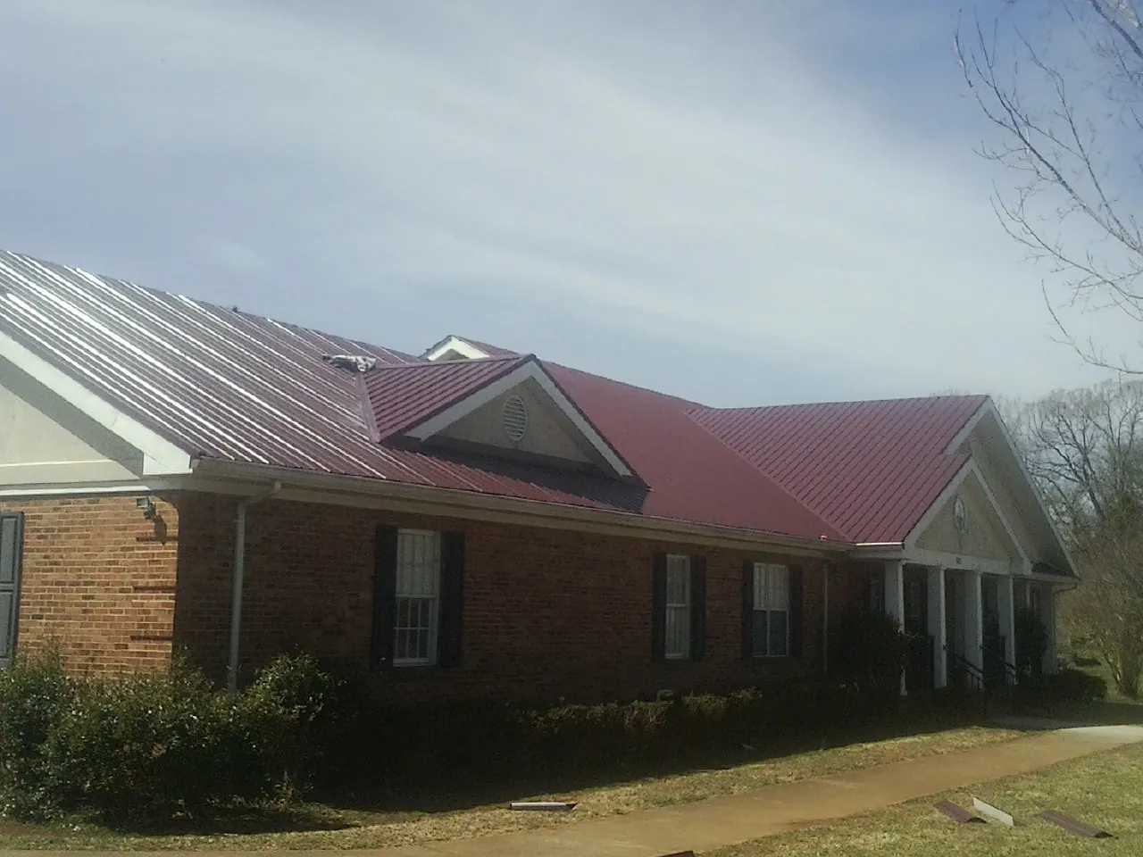 Red metal roof with gabled entries on a long brick building, from a Hail Damage Roof Repair job in Tussy