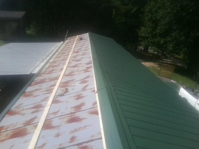 Old rusted panels beside newly installed green metal roofing — Wind Damage Roof Repair by Roofing Brothers in Tussy