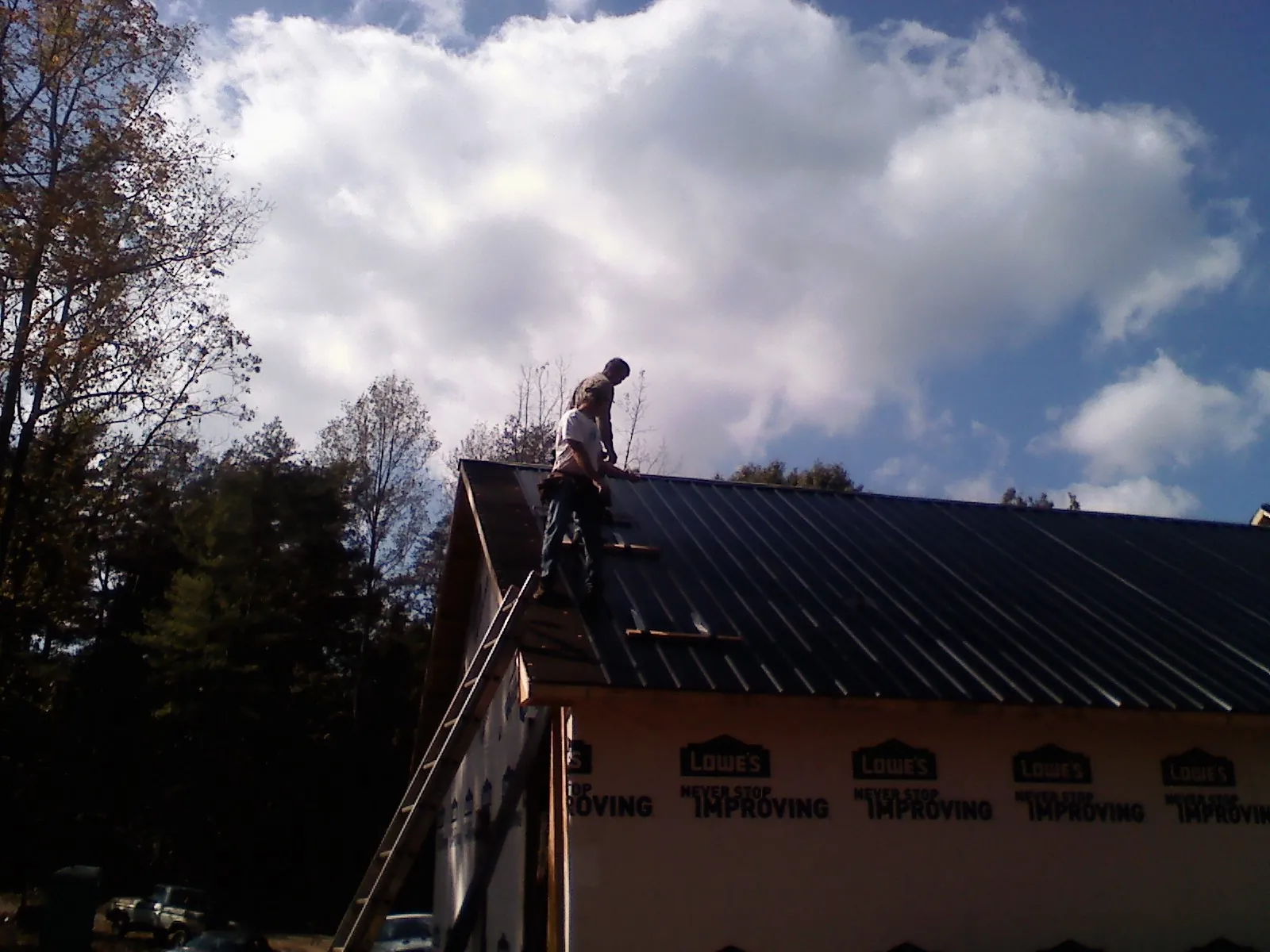 Roofer fastening dark metal panels high against a cloudy sky, from a Roof Inspection job in Tussy