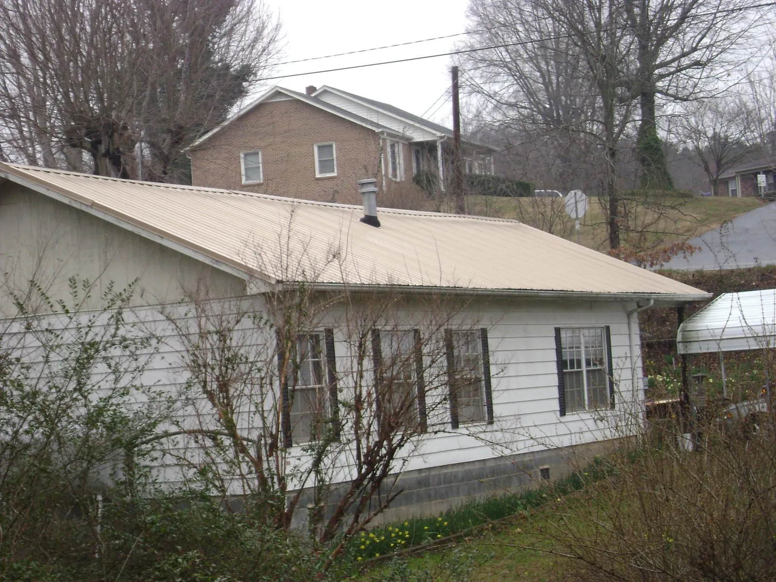 Tan metal roof on a white sided house set into a hillside — Commercial Roofing by Roofing Brothers in Tussy