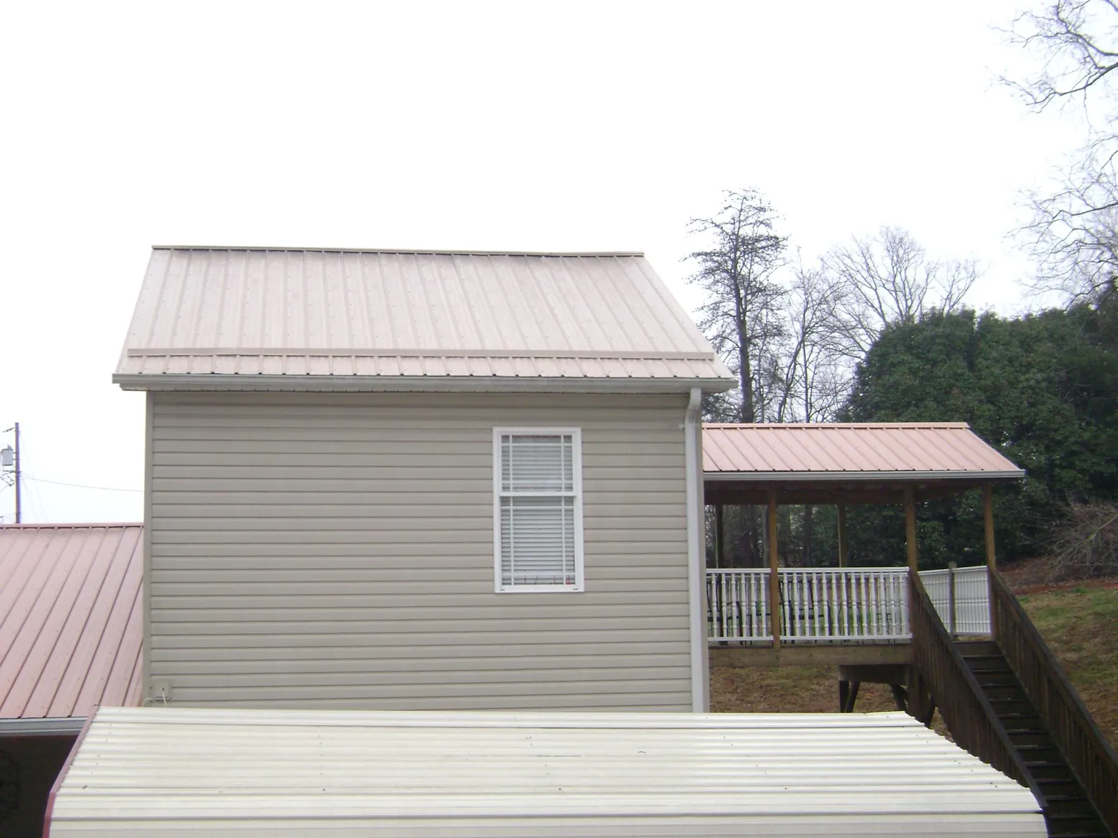 Tan metal roofs on a two story addition and attached porch, from a Roof Replacement job in Tussy